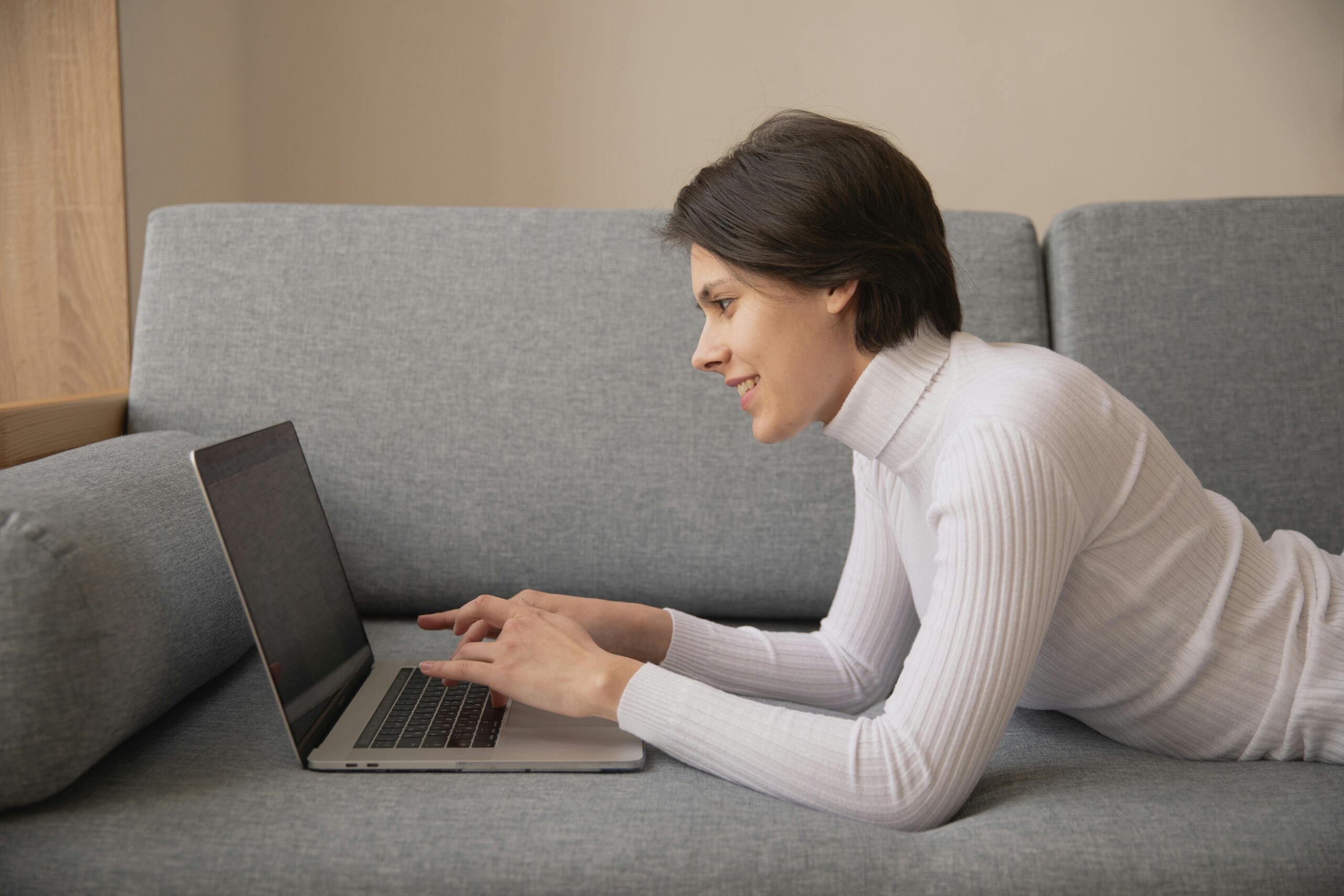 Woman working remotely on a laptop at home, lying on a comfortable sofa.